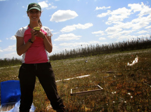 Woman standing in a wetland, grinning and holding out a handful of peat moss