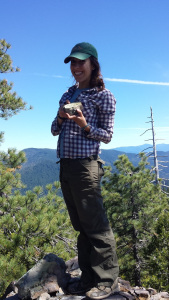 The same woman, two years later, wearing flannel on a mountain ridge. She is grinning and holding up a large rock.