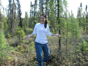 A young woman, smiling in a boreal black spruce forest.