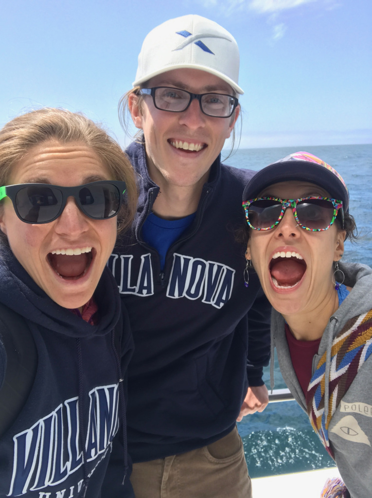Three smiling young adults taking a selfie on a whale watching boat