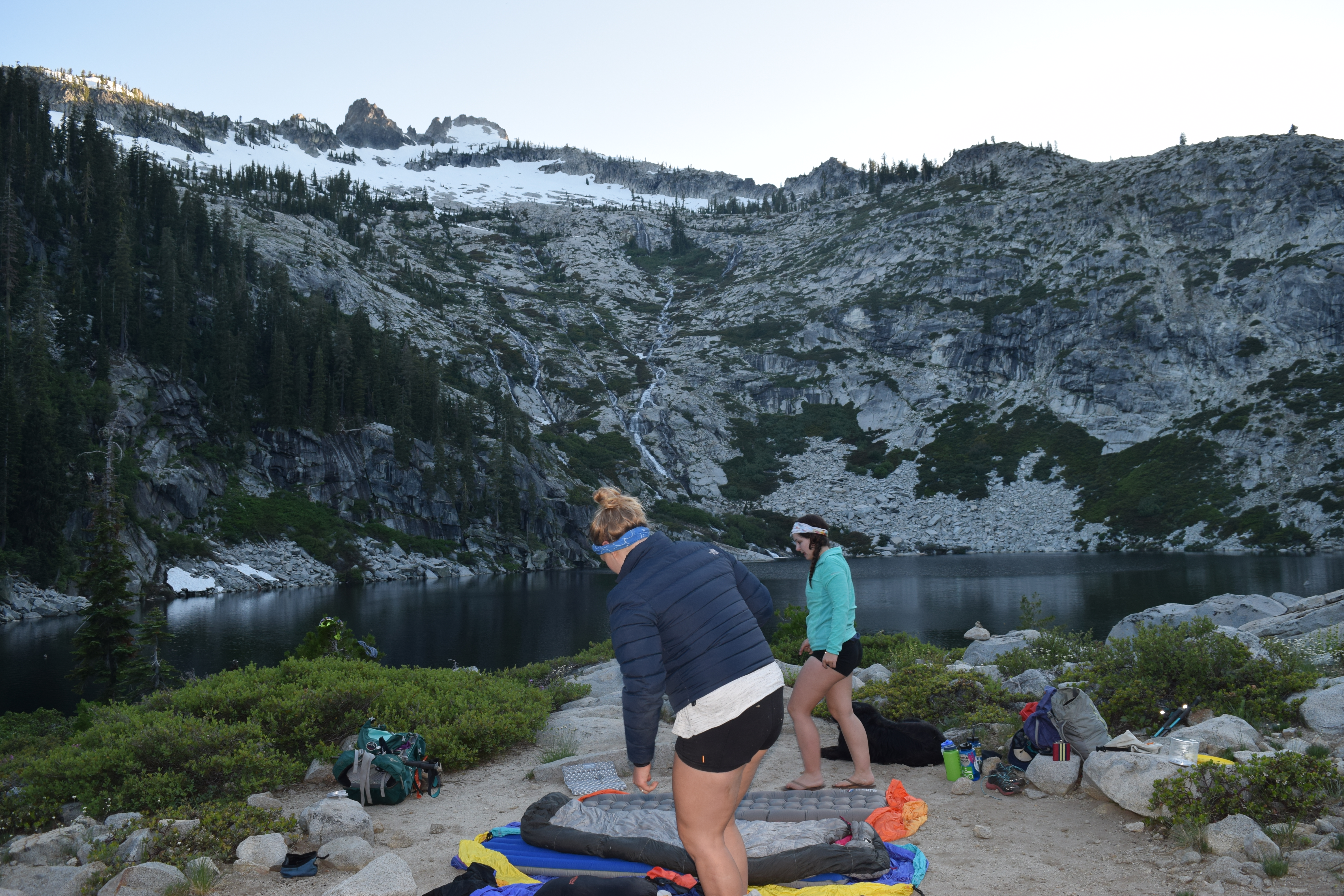 Two woman setting up a campsite overlooking a small lake in a mountain basin.