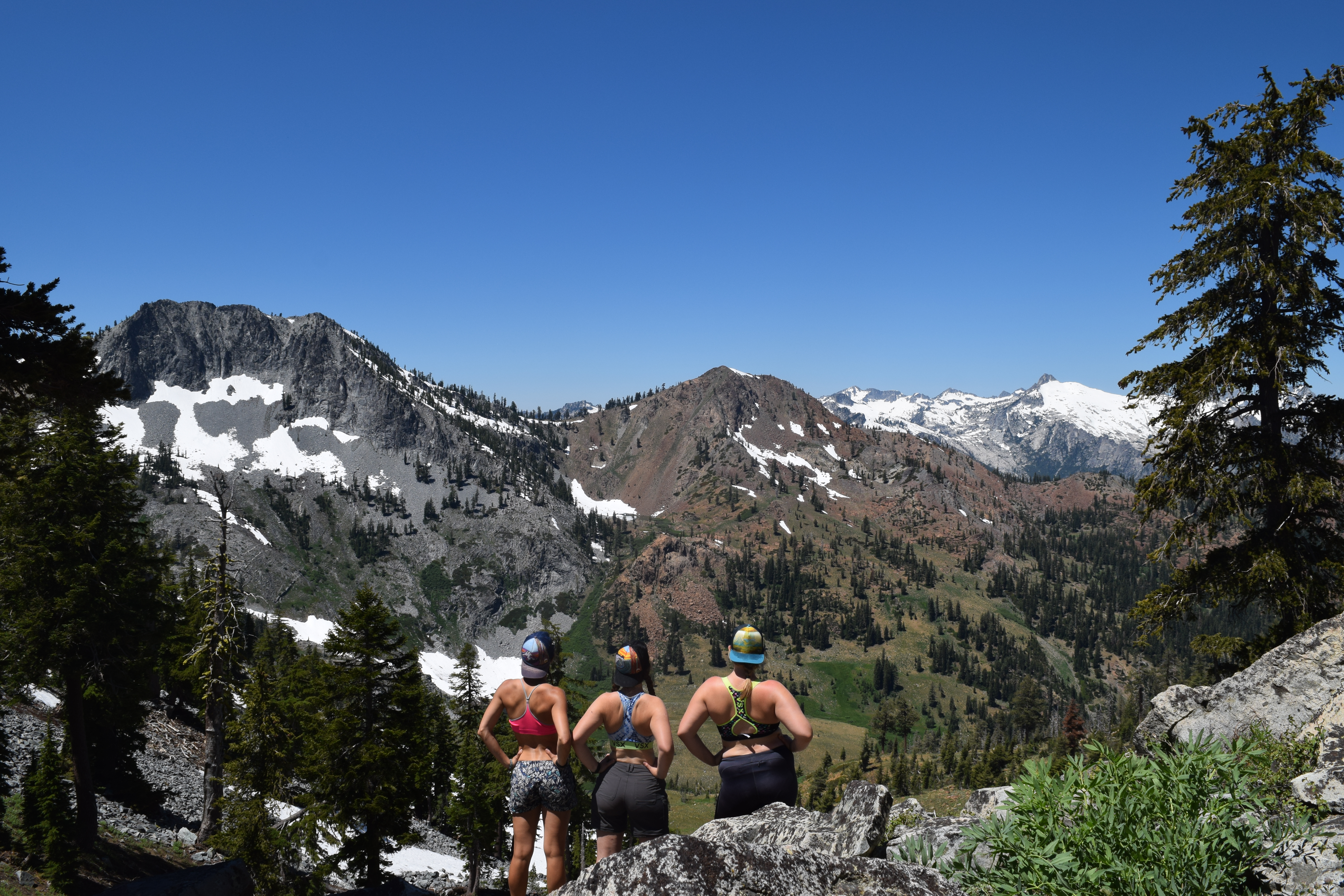 Three women in sports bras and shorts, looking out at a mountain basin whose rock types correspond very well to the above geologic map.